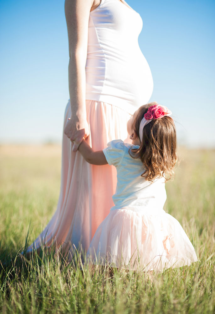 Child looking up at pregnant mother in sunshine