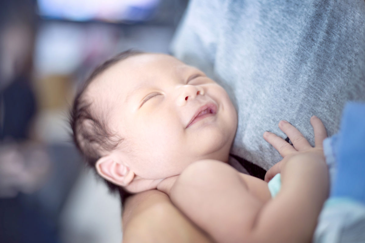 sleeping baby in mother's arms smiling with relaxed hands