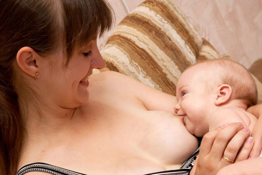 Baby with breast in mouth smiles at mother
