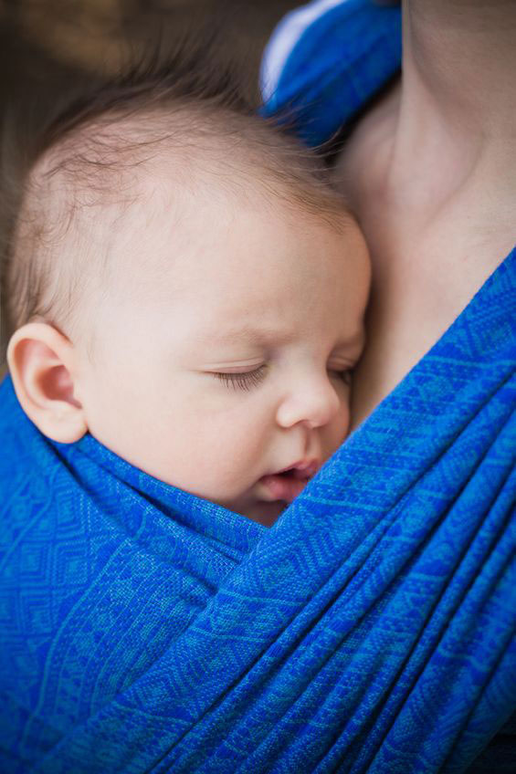 Little baby in a blue wrap on mother's chest