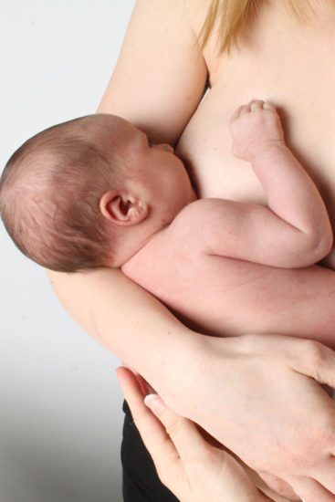 Mother holding baby to breastfeed while standing