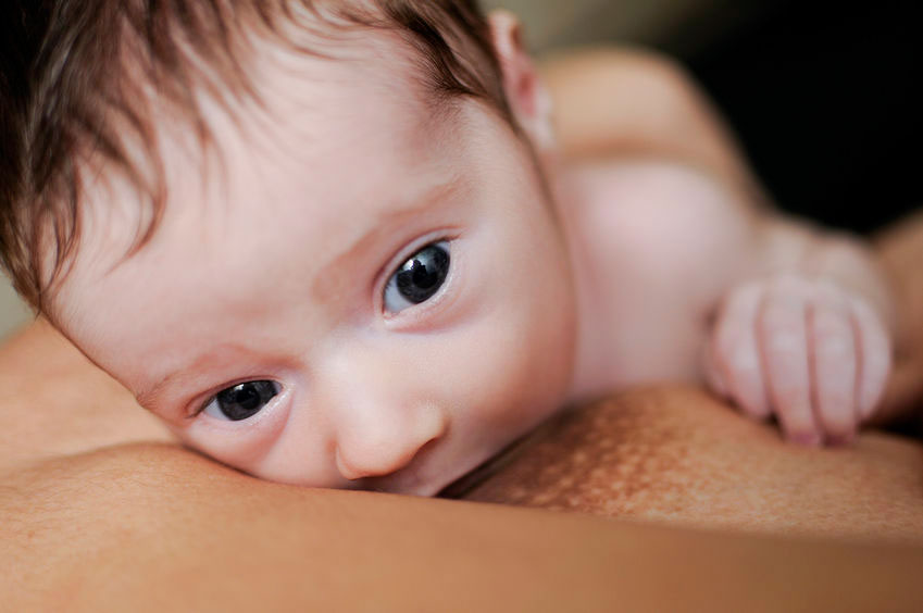 Cute baby looking towards camera while breastfeeding