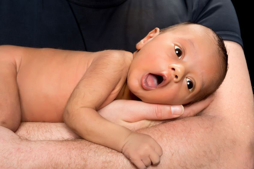 baby lying on father's hands with mouth open