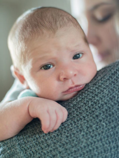 baby looking uncomfortable on mother's shoulder