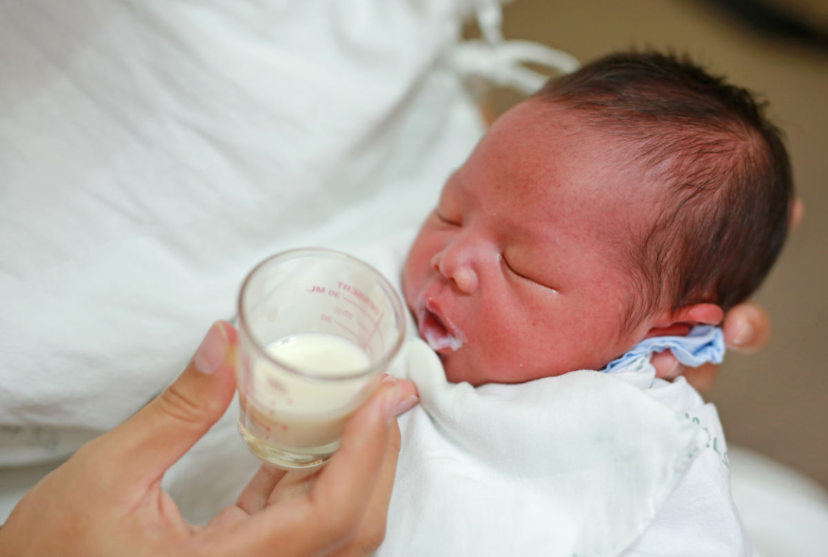 caregiver removes the cup from baby's lips as baby has closed his eyes and become sleepy