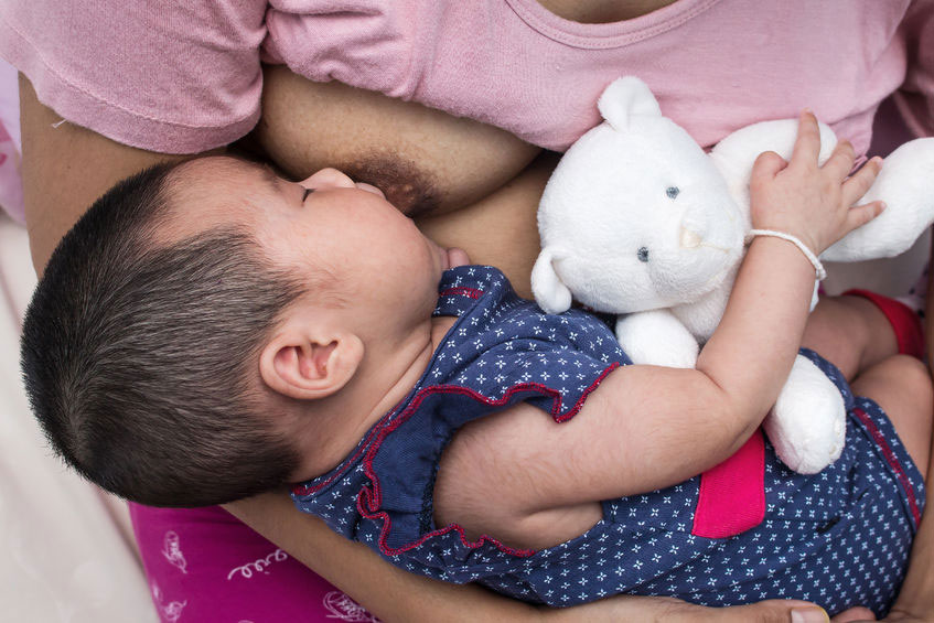 mother breastfeeding a baby who is holding a teddy