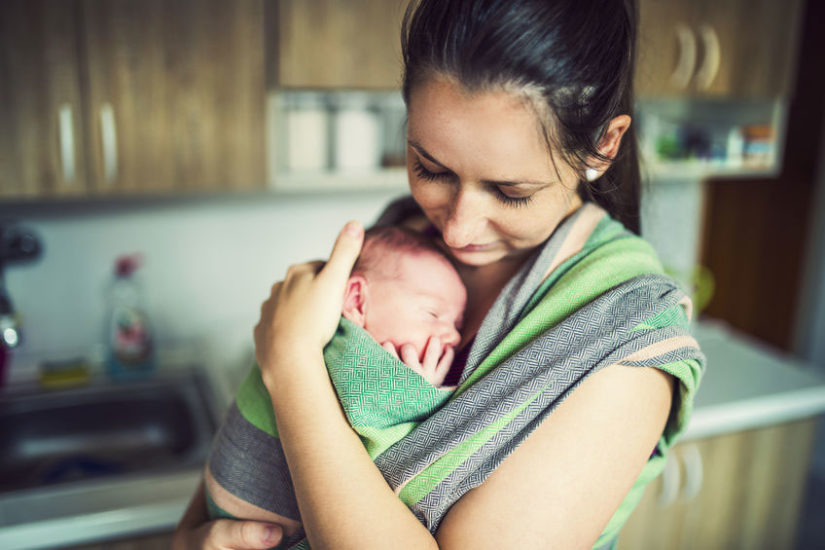 Baby held in a green wrap on mother's chest